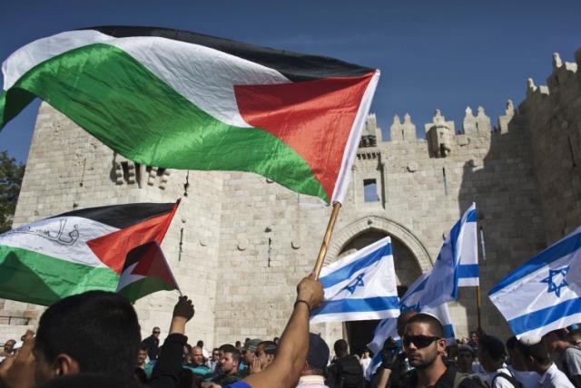 Palestinian protesters wave Palestinian flags as Israelis carrying Israeli flags walk past in front of the Damascus Gate outside Jerusalem's Old City (photo credit: REUTERS)