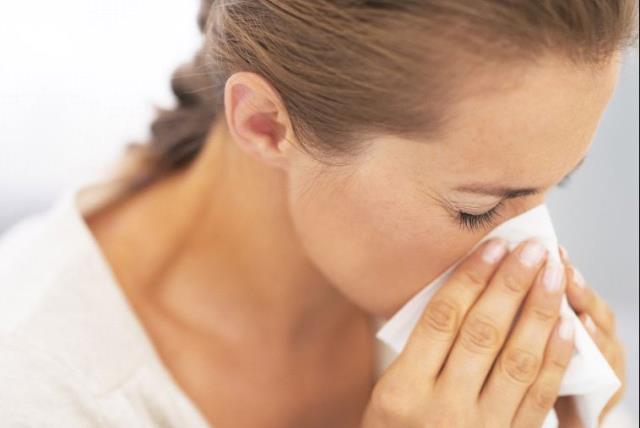 A woman blowing her nose into a tissue, possibly after or sneeze or while sick (photo credit: INGIMAGE)
