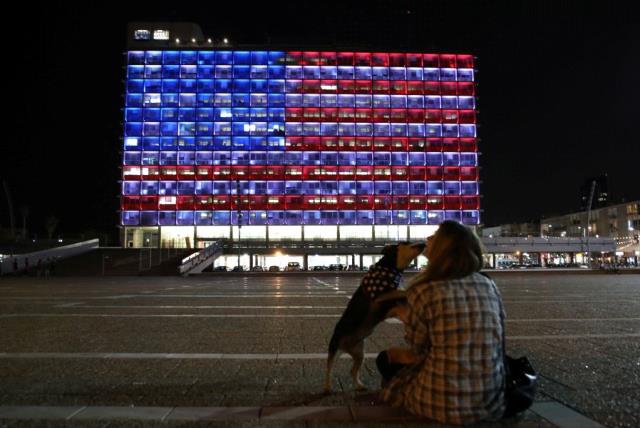 A woman plays with her dog as the municipality building is lit in the colours of the American flag on the first day of U.S. President Donald Trump's visit in Israel, in Tel Aviv, Israel May 22, 2017. (photo credit: REUTERS/CORINNA KERN)