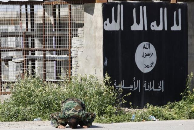A member of a militia kneels as he celebrates victory next to a wall painted with the black flag commonly used by ISIS militants (photo credit: REUTERS)
